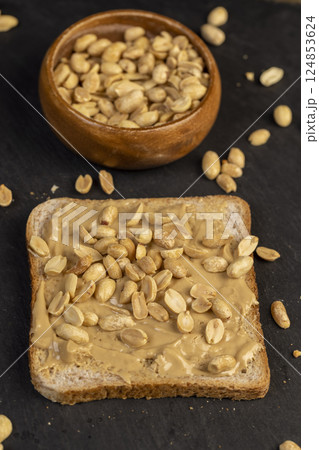 butter on a piece of bread and roasted peanuts on the table, closeup on black slate butter on a piece of bread and roasted peanuts on the table, closeup on black slate 124853624
