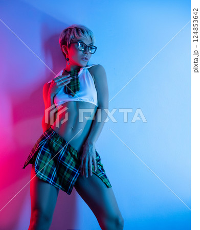 A sexy girl in an erotic school costume with a plaid skirt from a sex shop poses erotically on a neon background from a copy paste 124853642