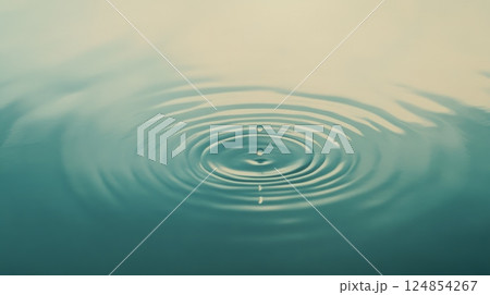 Dropping into tranquil water, creating expanding circular ripples that gracefully spread across the surface, evoking a soothing and meditative atmosphere of peace and purity 124854267