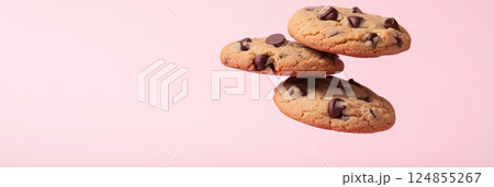 Three mouthwatering chocolate chip cookies levitating against a vibrant pink backdrop, creating an enticing and visually striking image perfect for dessert lovers and food enthusiasts 124855267