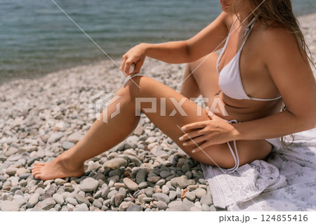 A woman is sitting on a beach with her legs crossed and a bottle of sunscreen in her hand. A woman is sitting on a beach with her legs crossed and a bottle of sunscreen in her hand. 124855416