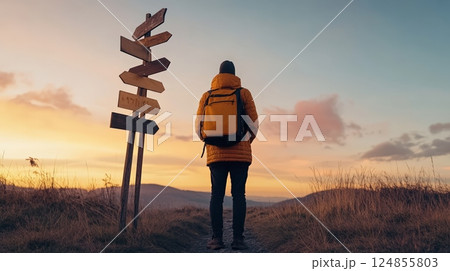 Hiker with a backpack contemplating directions at sunset near a signpost, representing choices, opportunities, and the fear of better options 124855803