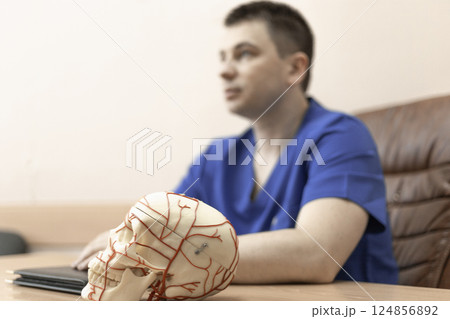 model of a human skull, in the background a doctor man is a blurred silhouette model of a human skull, in the background a doctor man is a blurred silhouette 124856892