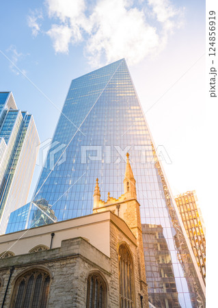St Andrew Undershaft Church stands in contrast to the sleek skyscrapers of London's financial district. The sunlight reflects off the glass buildings surrounding this historic site. 124856919