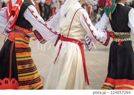 Women in traditional folk costumes dancing in circle at a cultural Bulgarian festival. Close-up of hands joined during traditional folk dance. Vibrant embroidered outfits, national traditions Women in traditional folk costumes dancing in circle at a cultural Bulgarian festival. Close-up of hands joined during traditional folk dance. Vibrant embroidered outfits, national traditions 124857264