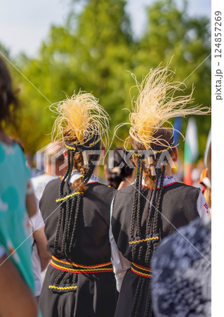 Women in traditional Bulgarian folk costumes with braided hair and feather headpieces, outdoor event. Bulgarian traditions. Folk outfit expresses identity, roots, cultural heritage Women in traditional Bulgarian folk costumes with braided hair and feather headpieces, outdoor event. Bulgarian traditions. Folk outfit expresses identity, roots, cultural heritage 124857269