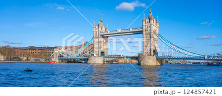 Tower Bridge stands majestically over the River Thames, showcasing its stunning architecture against a clear blue sky. Visitors enjoy the vibrant atmosphere along the waterfront. 124857421