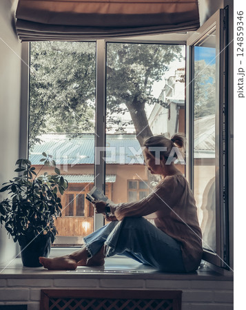 Woman reading a book sitting on the windowsill Woman reading a book sitting on the windowsill 124859346