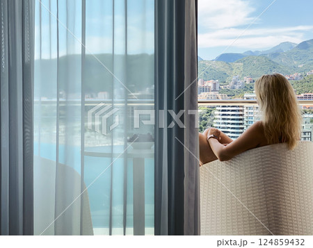 A woman sits on a balcony enjoying the view of the sea and mountains A woman sits on a balcony enjoying the view of the sea and mountains 124859432