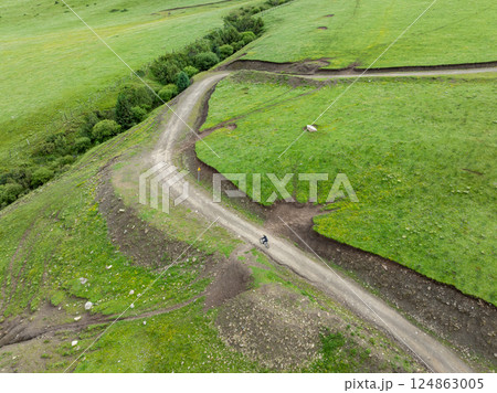 Aerial view of woman riding mountain bike on flowering grassland mountain trail 124863005