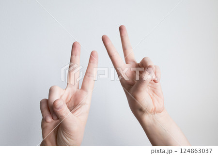 Caucasian hands displaying peace sign gestures against light background Caucasian hands displaying peace sign gestures against light background 124863037