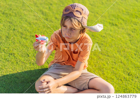 Boy wearing a pilot hat running through the grass with a toy airplane, dreaming of adventures. Childhood, imagination, and freedom concept Boy wearing a pilot hat running through the grass with a toy airplane, dreaming of adventures. Childhood, imagination, and freedom concept 124863779