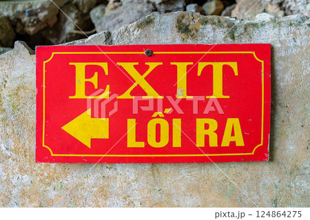 A close-up shows a red exit sign with Vietnamese translation, mounted on a weathered wall. It directs visitors to the exit. A close-up shows a red exit sign with Vietnamese translation, mounted on a weathered wall. It directs visitors to the exit. 124864275