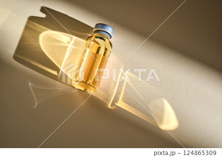 Injection vial with medicinal product in sunlight on beige background. 124865309