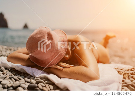 A woman sunbathes on the beach, lying on her stomach in a red swimsuit against the sea backdrop. 124865476