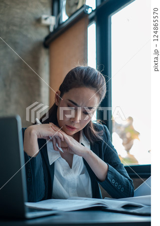 Professional woman in office attire deeply focused on reviewing documents by a window, showcasing concentration and business environment. Professional woman in office attire deeply focused on reviewing documents by a window, showcasing concentration and business environment. 124865570