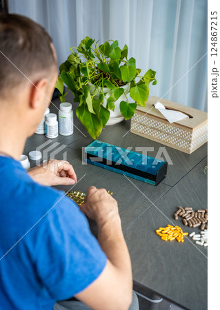 Man sorting his pills and supplements into a weekly pill organizer. Concept of medication management and daily health routine Man sorting his pills and supplements into a weekly pill organizer. Concept of medication management and daily health routine 124867215