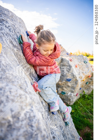 Little girl climbing an artificial climbing wall in a playground, developing strength and coordination Little girl climbing an artificial climbing wall in a playground, developing strength and coordination 124868380