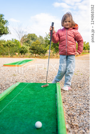 Little girl playing mini golf outdoor. Child having fun with new activity in spring time. Family vacations or resort. Little girl playing mini golf outdoor. Child having fun with new activity in spring time. Family vacations or resort. 124868382