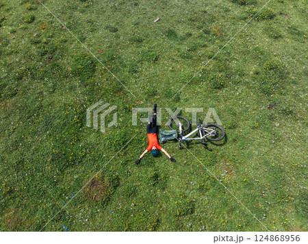 Aerial view of woman cyclist with mountain bike on flowering grassland mountain 124868956