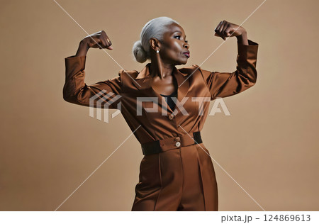 middle age woman feeling happy, satisfied and powerful, flexing fit and muscular biceps, looking strong after the gym against yellow wall 124869613
