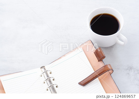 淹れたてのコーヒーを飲みながら、リング式のシステム手帳を開いてデスクワークをしているイメージ 淹れたてのコーヒーを飲みながら、リング式のシステム手帳を開いてデスクワークをしているイメージ 124869657
