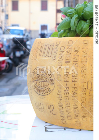 Large head of parmesan cheese with basil on table in street oudoor. Traditions and food, Italy.  124869799