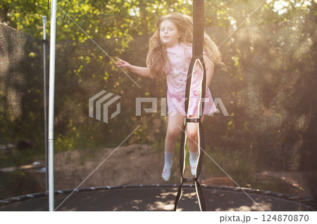 Child girl jumping on trampoline outdoors in the yard on summer vacation. Child girl jumping on trampoline outdoors in the yard on summer vacation. 124870870