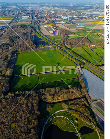 Aerial view of scenic farmland near the coast with colorful flower fields, dense forests, and circular ponds in a landscaped park. The North Sea is visible in the distance under a clear sky. Aerial view of scenic farmland near the coast with colorful flower fields, dense forests, and circular ponds in a landscaped park. The North Sea is visible in the distance under a clear sky. 124870980