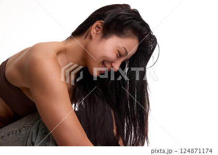 Portrait of young Korean woman in top and jeans, with long black hair and smooth, clear face without makeup, smiling against white background. Portrait of young Korean woman in top and jeans, with long black hair and smooth, clear face without makeup, smiling against white background. 124871174