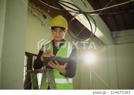 Professional electrician reviewing plans and making notes while conducting an electrical inspection Professional electrician reviewing plans and making notes while conducting an electrical inspection 124873361