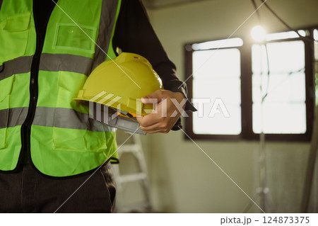 Engineer in a safety vest holding yellow hard hat at a construction site 124873375