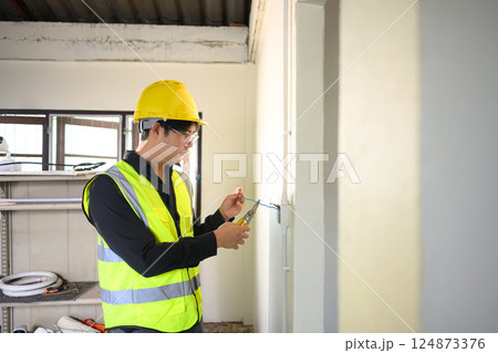 Electrician wearing yellow hard hat working on wall wiring at a construction site Electrician wearing yellow hard hat working on wall wiring at a construction site 124873376