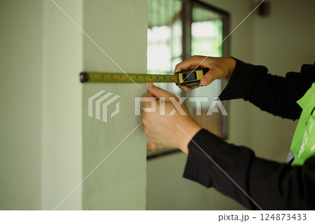 Close up of worker using measuring tape to check wall dimensions at a construction site 124873433