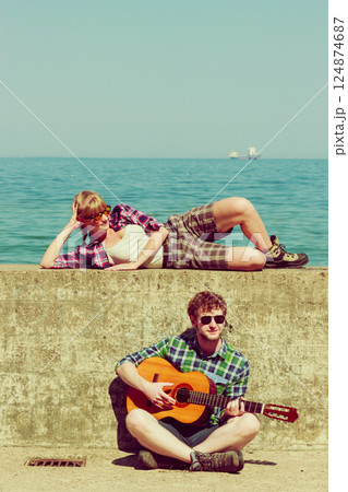 Young man playing guitar to his girlfriend by seaside 124874687