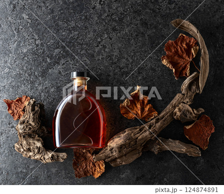 Bottle of brandy and old snags with dried up vine leaves. 124874891