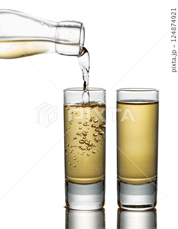 Gold liquor pouring into a glass on a white background. 124874921