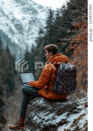 Man during hike sitting on a rock with a laptop on his lap. Remote work. A man finds a peaceful spot on a rock, using his laptop to stay productive while hiking in the great outdoors. 124875365