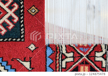 Manufacturing process, weaving of a traditional wool oriental red carpet with an intricate floral pattern, decorative elements 124875478