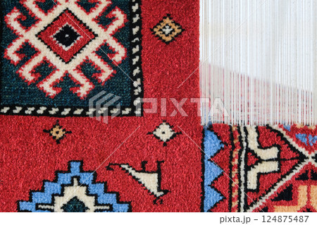 Manufacturing process, weaving of a traditional wool oriental red carpet with an intricate floral pattern, decorative elements Manufacturing process, weaving of a traditional wool oriental red carpet with an intricate floral pattern, decorative elements 124875487
