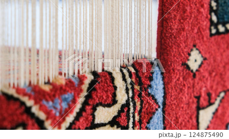 Manufacturing process, weaving of a traditional wool oriental red carpet with an intricate floral pattern, decorative elements Manufacturing process, weaving of a traditional wool oriental red carpet with an intricate floral pattern, decorative elements 124875490