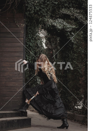 Woman in dark vintage gown stepping onto wooden porch, dagger hidden in boot. Fantasy characters. Suitable for thriller or dark fantasy cover. 124875533