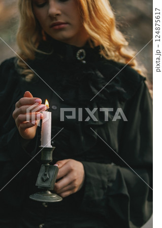 Close-up of woman's hand lighting candle, dressed in vintage black blouse, symbolic of ritual, remembrance or hidden secrets. 124875617