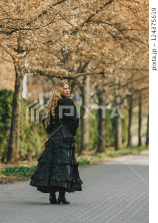 Young woman in black Victorian dress walking through autumn park, glancing back with suspicion. Concept of vintage Young woman in black Victorian dress walking through autumn park, glancing back with suspicion. Concept of vintage 124875619