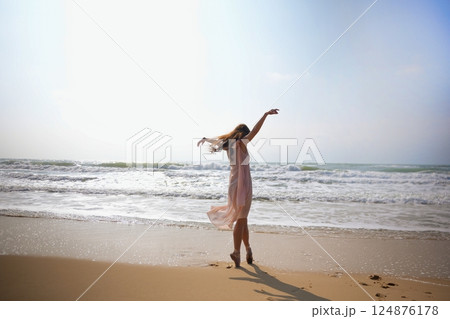 Light dress flows as ballerina stands en pointe on surfboard in ocean breeze Light dress flows as ballerina stands en pointe on surfboard in ocean breeze 124876178