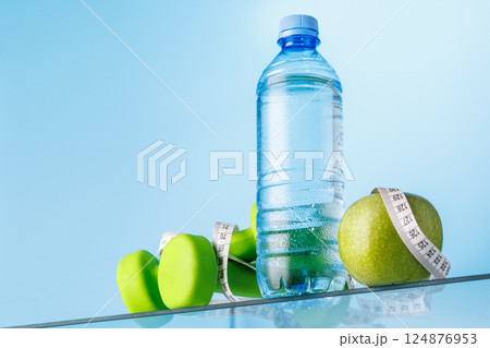 Bottle of water, green apple, and dumbbells on a glass table 124876953