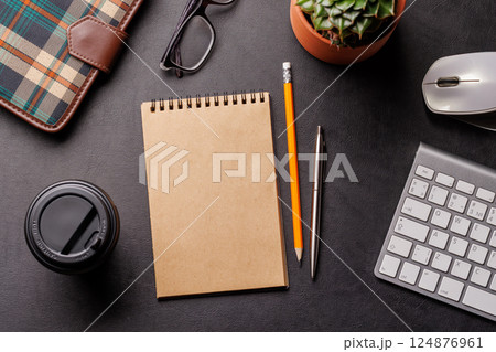 Top view of a dark leather office desk with notepad, supplies, and coffee cup 124876961