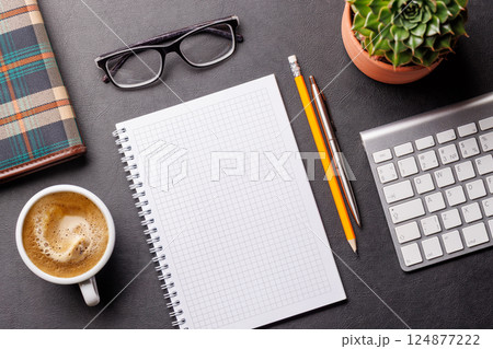 Top view of a dark leather office desk with notepad, supplies, and coffee cup 124877222