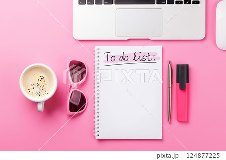 Stylish pink desk with laptop, coffee cup, office supplies, and a notepad for writing a to-do list Stylish pink desk with laptop, coffee cup, office supplies, and a notepad for writing a to-do list 124877225