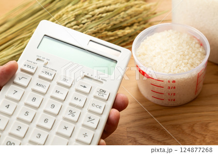 計量カップに入った米と電卓を持つ手元 124877268